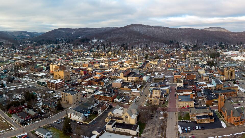 A cityscape with a mix of historic and modern buildings, surrounded by mountains and a cloudy sky.