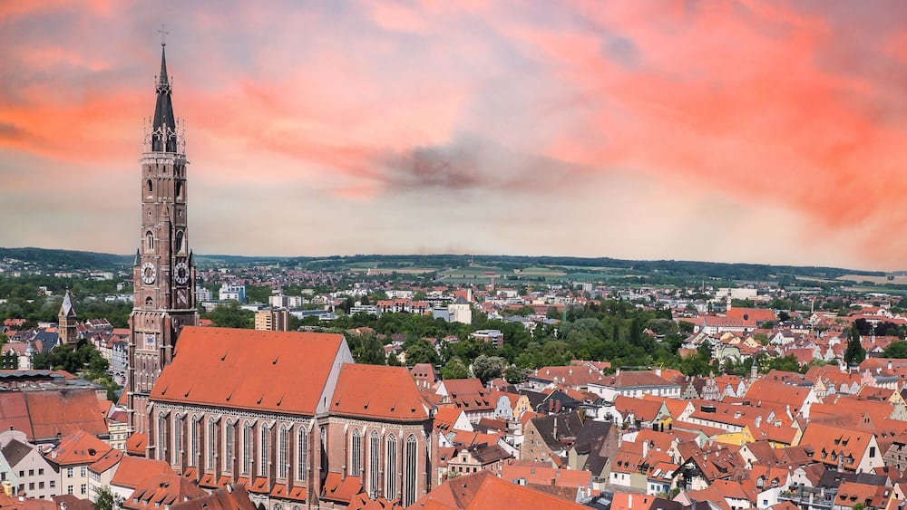Une vue urbaine avec un clocher d’église imposant, entouré de bâtiments aux toits rouges et sous un ciel nuageux.