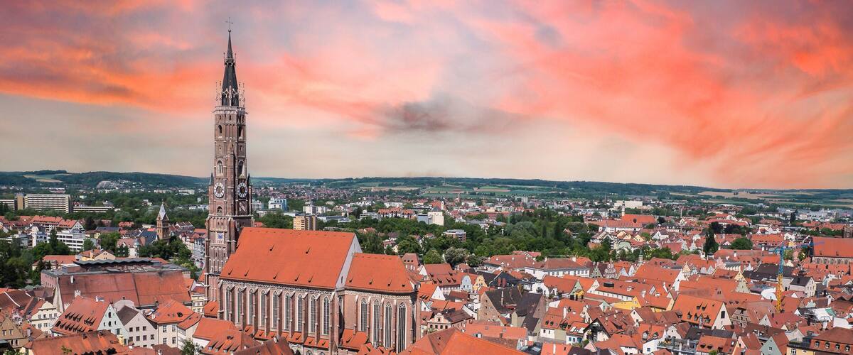 A cityscape with a prominent church tower, surrounded by red-roofed buildings and a cloudy sky.