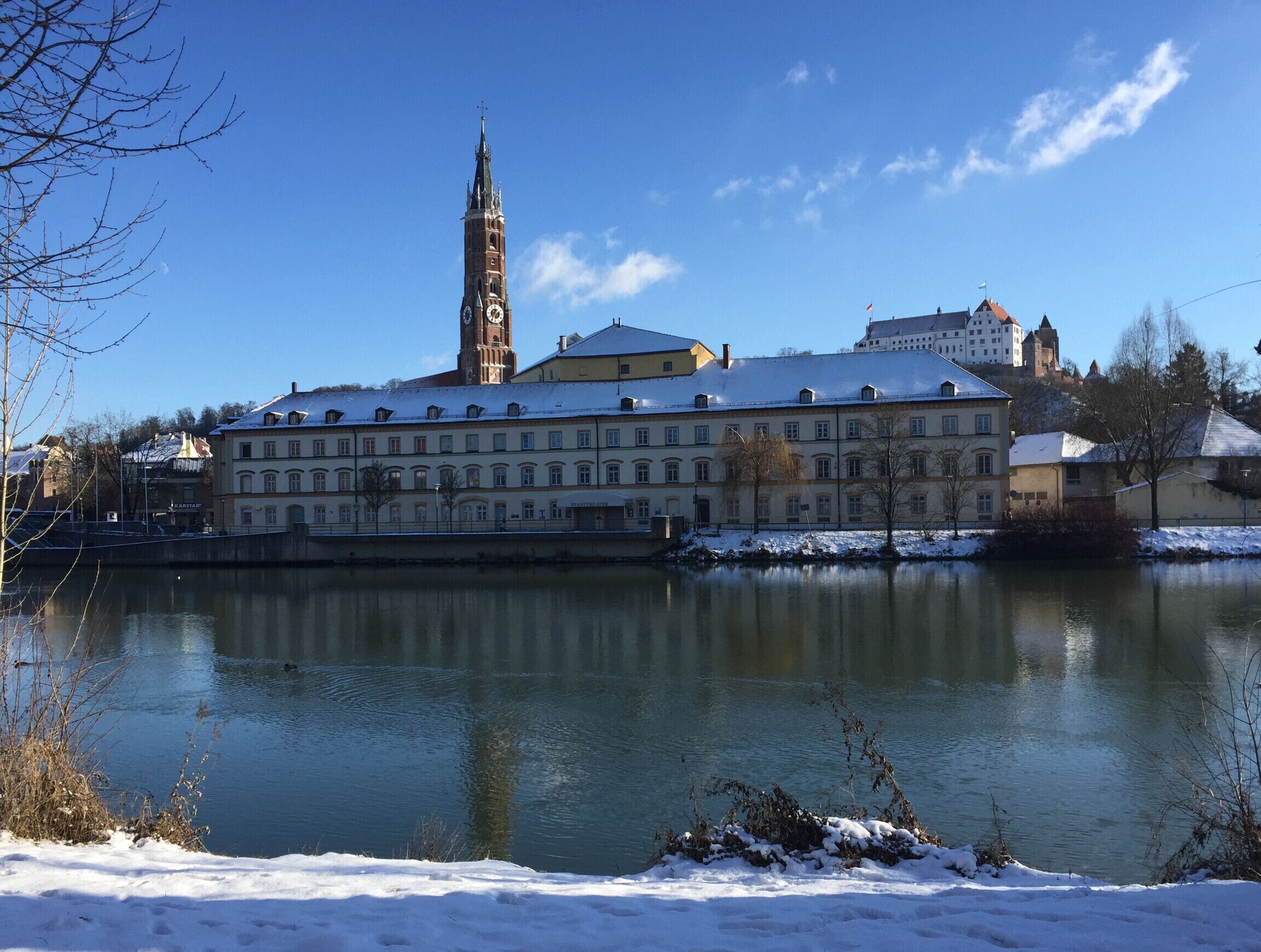 A historic building with a clock tower, a river, and snow-covered surroundings.