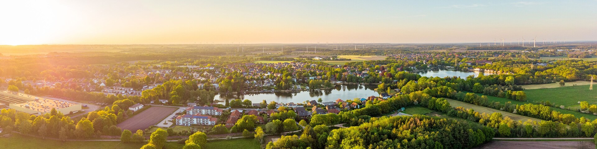 A rural landscape with a lake, wind turbines, and a residential area.