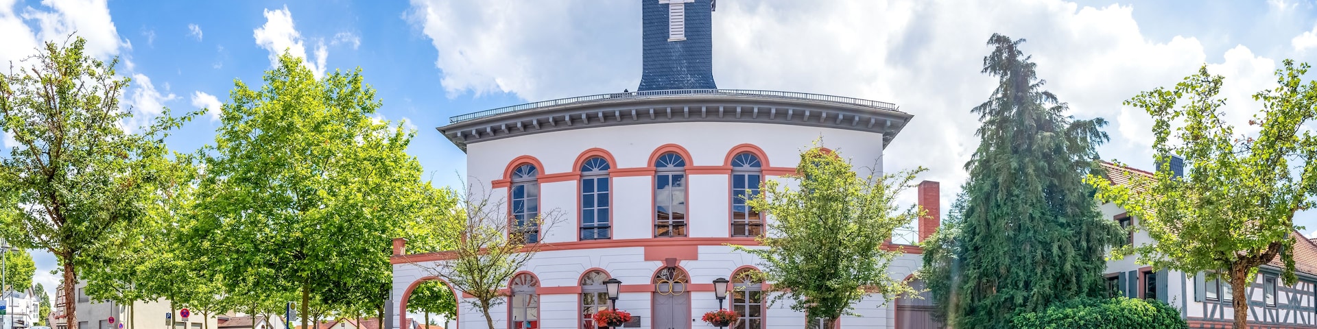 A historic building with a tower, surrounded by trees and parked cars.
