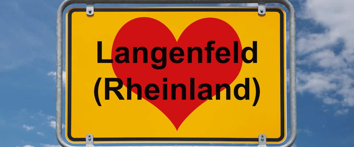 A yellow sign with a red heart and the text "Langenfeld (Rheinland)" against a blue sky with clouds.