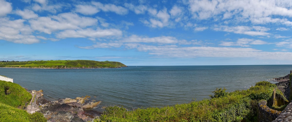 A lighthouse, grassy hills, and a calm sea under a partly cloudy sky.