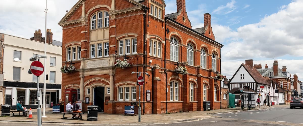 A historic red brick building with a clock tower, arched windows, and hanging flower baskets.