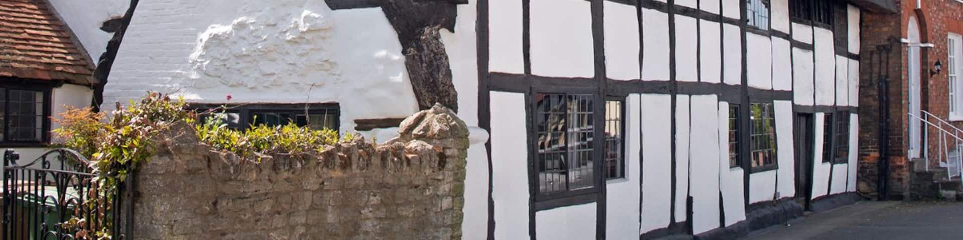 A traditional half-timbered house with a steeply pitched thatched roof and a brick chimney.