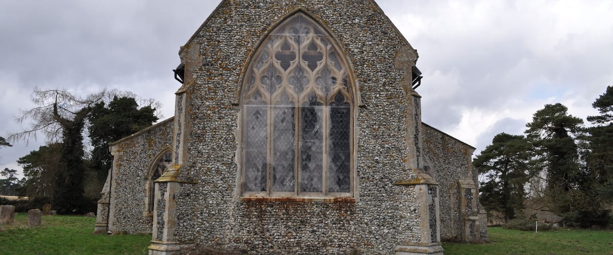 A stone church with a pointed roof and a large arched window.
