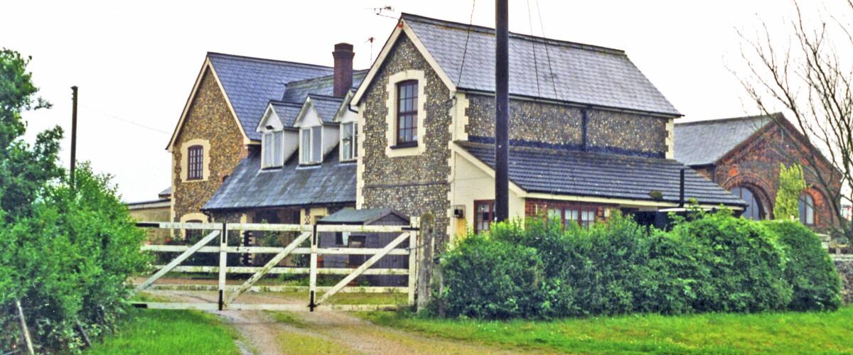 A stone house with a wooden gate, surrounded by greenery.