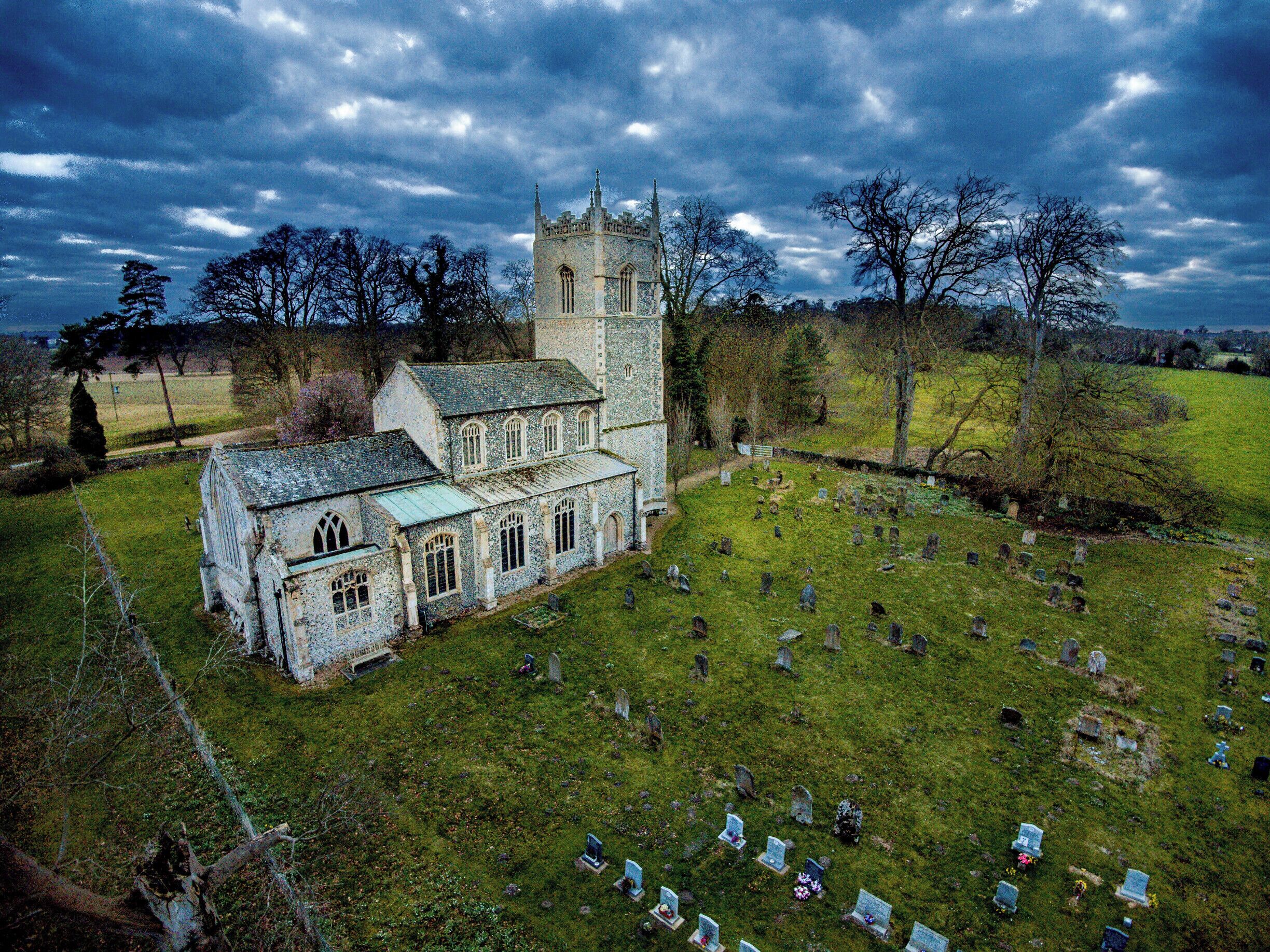 Eine historische Kirche mit einem Turm und einem Friedhof mit zahlreichen Grabsteinen.