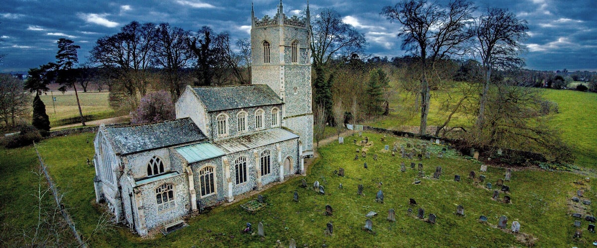 A historic church with a tower and a cemetery with numerous headstones.