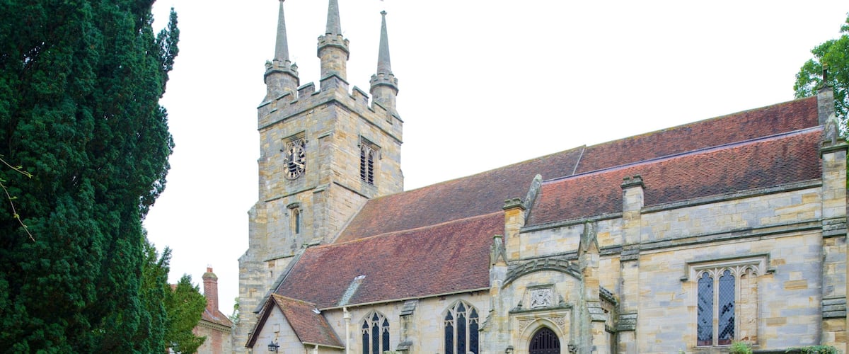 A historic church with a clock tower, stone walls, and a grassy cemetery.
