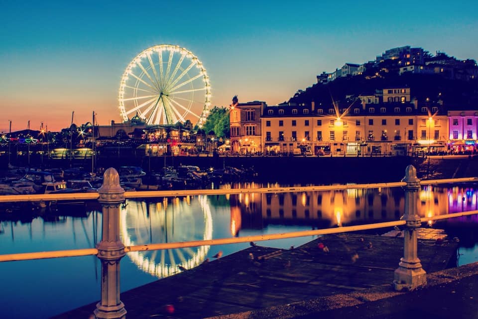 Ein Ufer mit einem großen Riesenrad, einer Brücke und Gebäuden entlang der Küste.