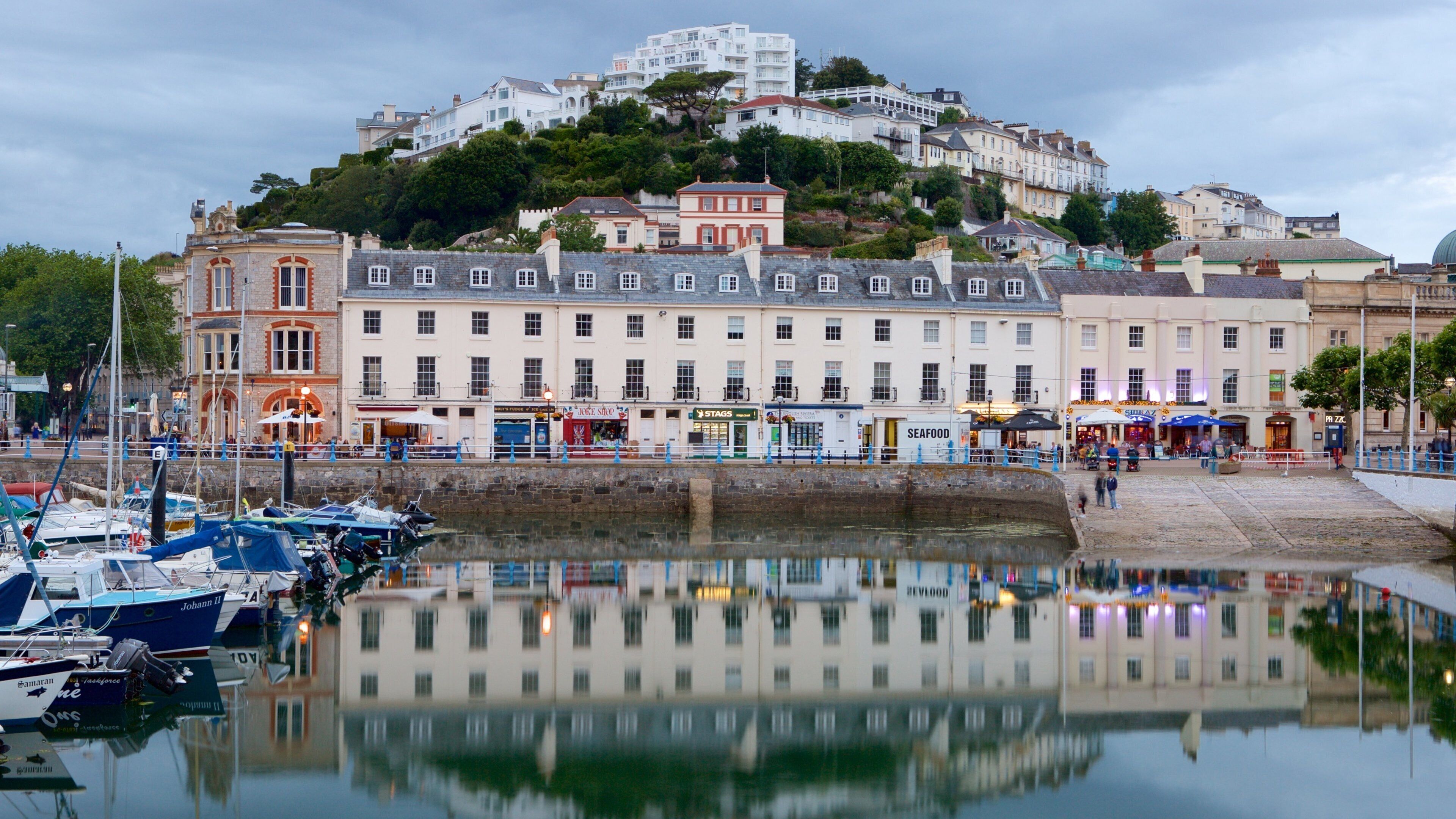 A harbor with boats, a waterfront promenade, and buildings with shops and restaurants.
