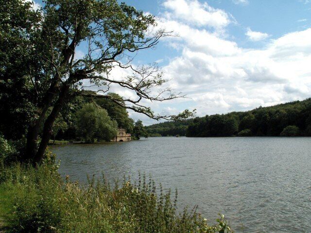 A calm lake with a tree on the left and a building in the distance.