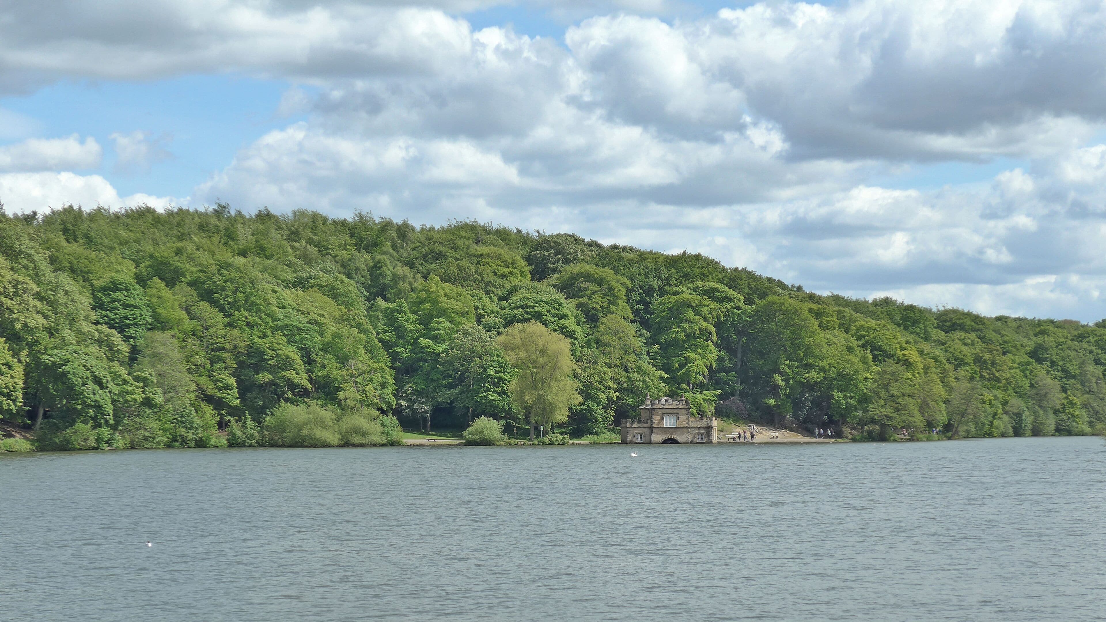 A lake with a forested hill and a stone building on the shore.