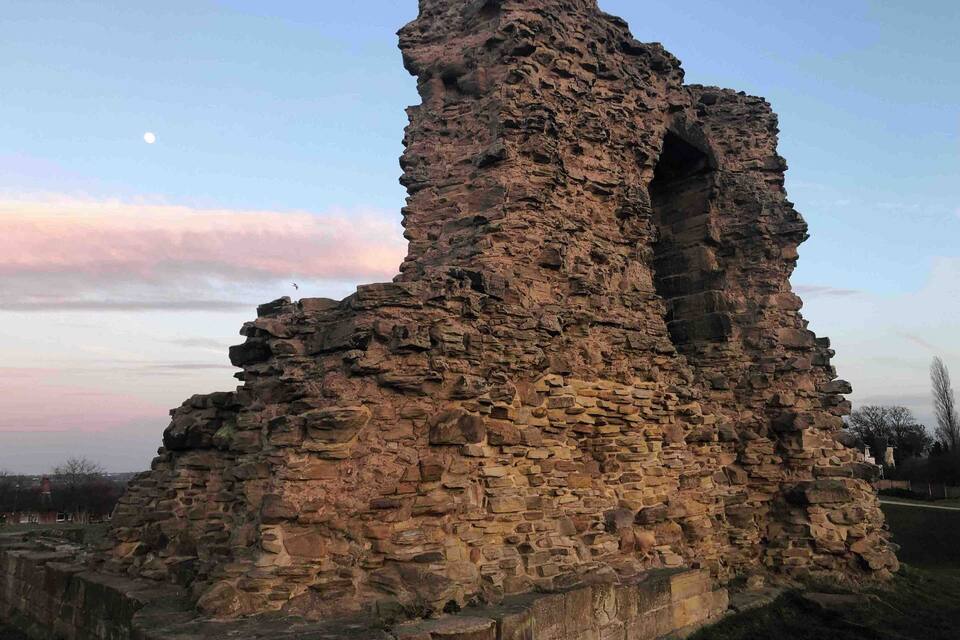 Una gran estructura de piedra antigua con un arco destacado, rodeada de césped y un cielo despejado.