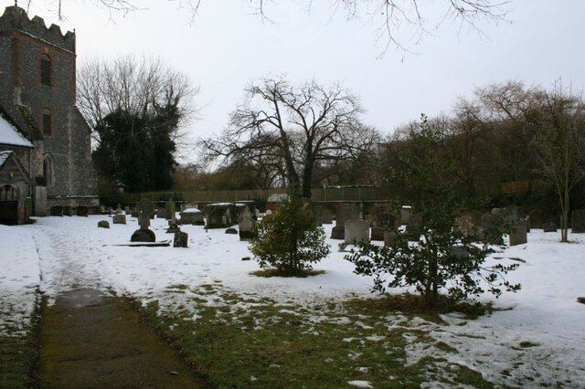 A church with a stone tower, a snow-covered cemetery, and leafless trees.