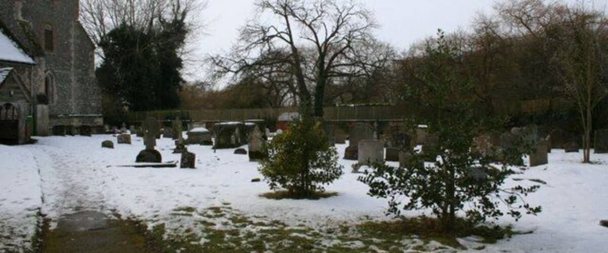 A church with a stone tower, a snow-covered cemetery, and leafless trees.