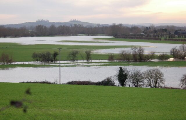 A flooded rural landscape with fields and a distant hill.
