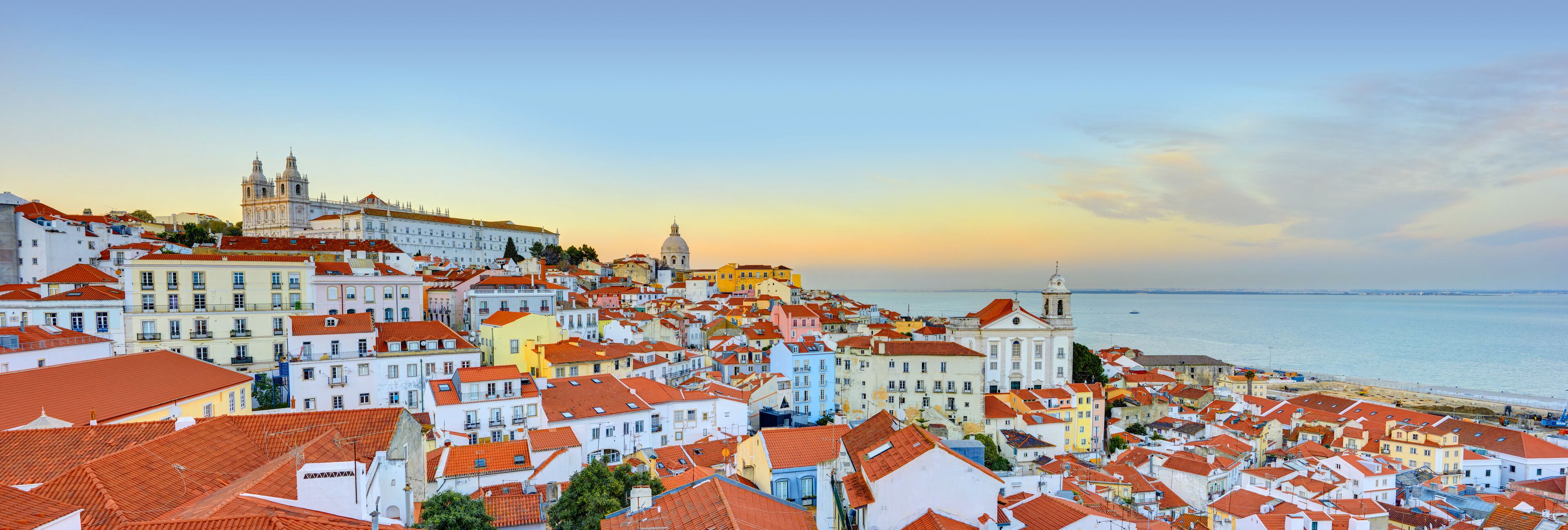 A coastal cityscape with colorful buildings, a prominent cathedral, and a beach in the background.