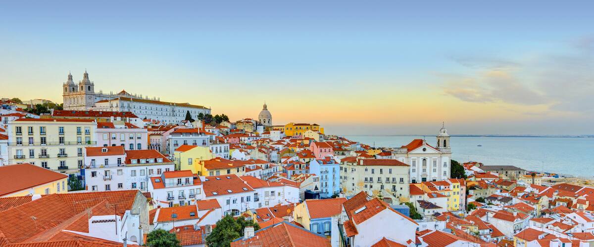 A coastal cityscape with colorful buildings, a prominent cathedral, and a beach in the background.