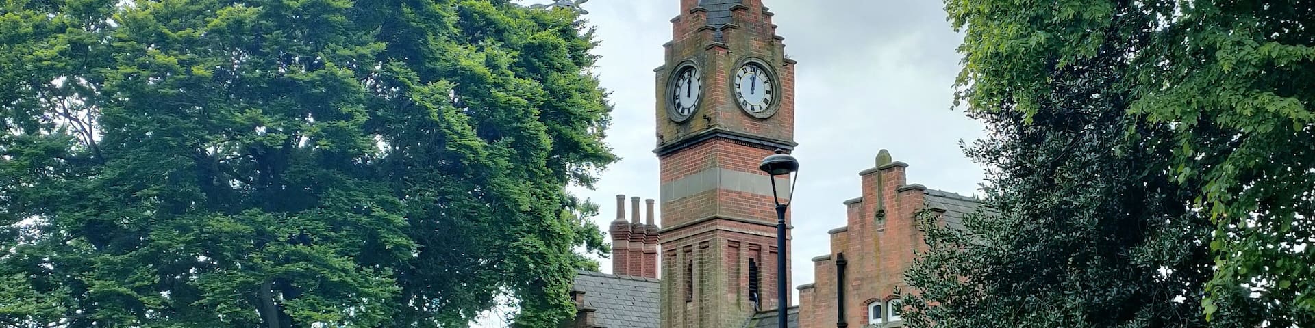A historic building with a clock tower, surrounded by lush greenery and a pathway.