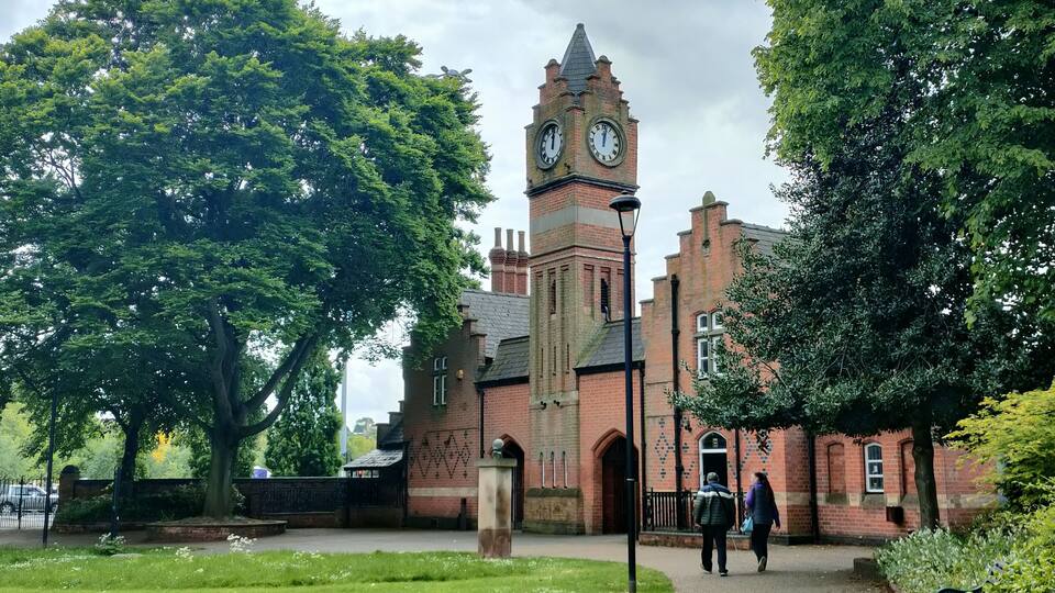 A historic building with a clock tower, surrounded by lush greenery and a pathway.