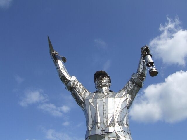 A metallic statue of a person holding a telescope and a book against a blue sky.