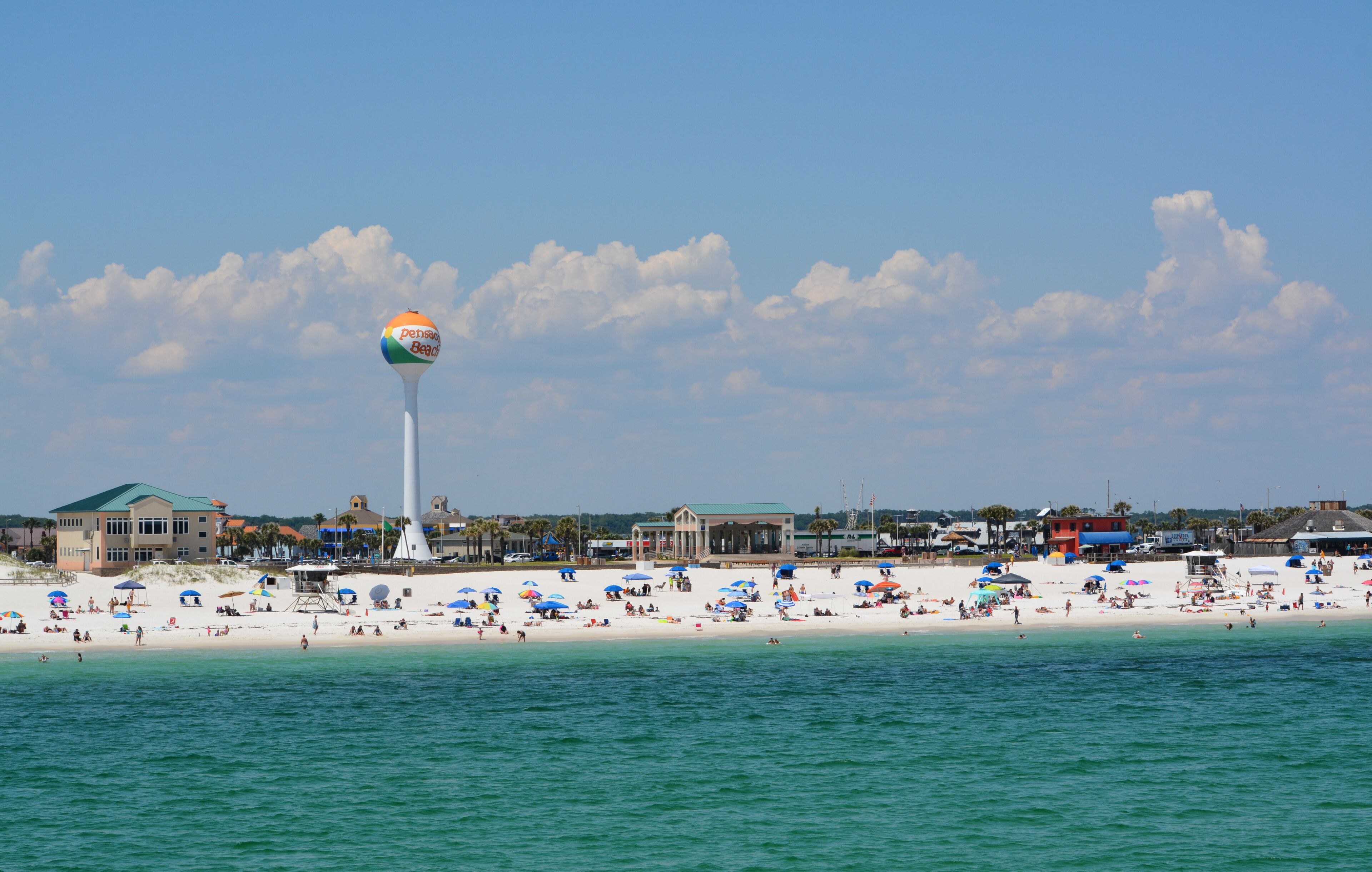 Une plage avec un grand château d’eau, un ciel bleu dégagé et une rive sablonneuse.