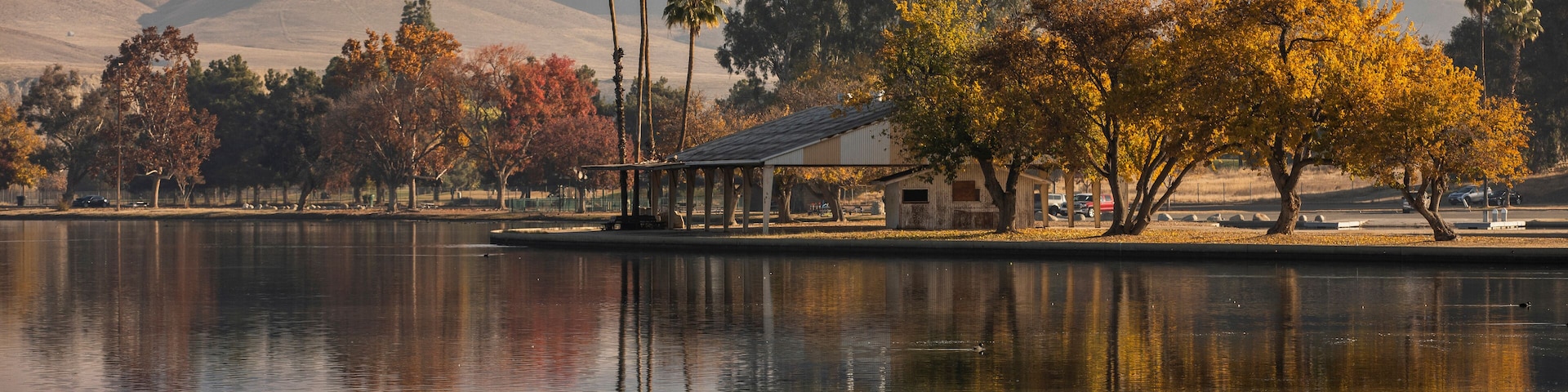 A calm lake with reflections of trees and a small building, surrounded by rolling hills.