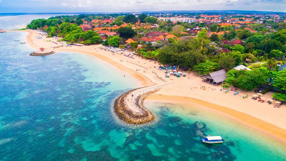 A coastal town with a sandy beach, clear turquoise waters, and red-roofed buildings.