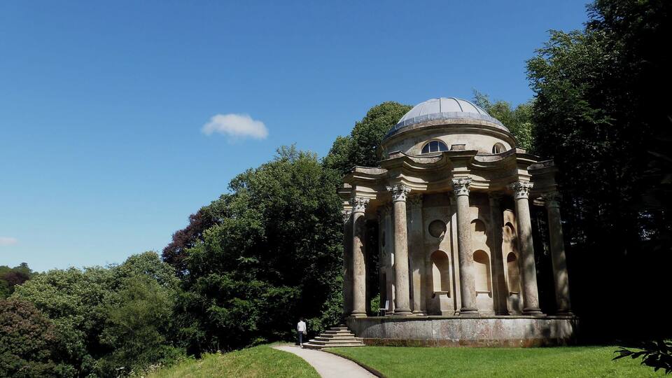 A classical building with a dome and columns, surrounded by lush greenery and a clear blue sky.