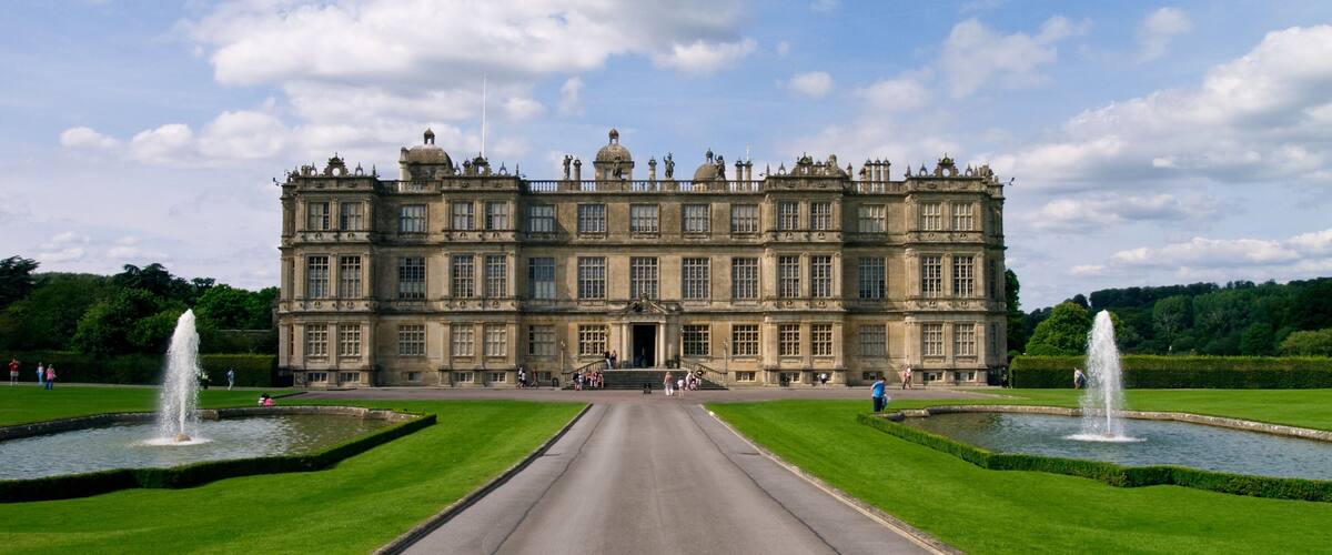 A large historic building with symmetrical gardens and fountains.