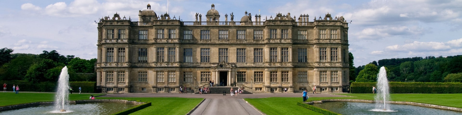 A large historic building with symmetrical gardens and fountains.