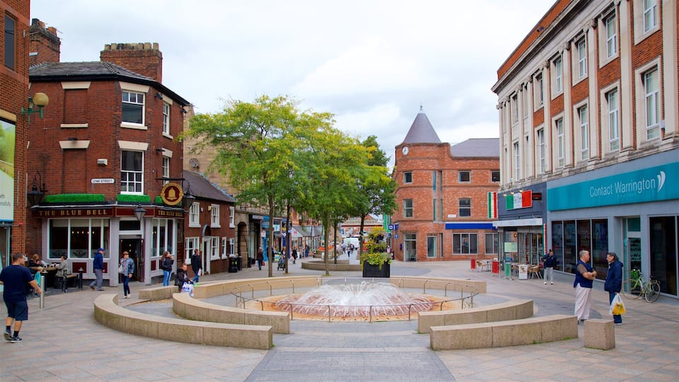 A public square with a central fountain, surrounded by brick buildings and shops.