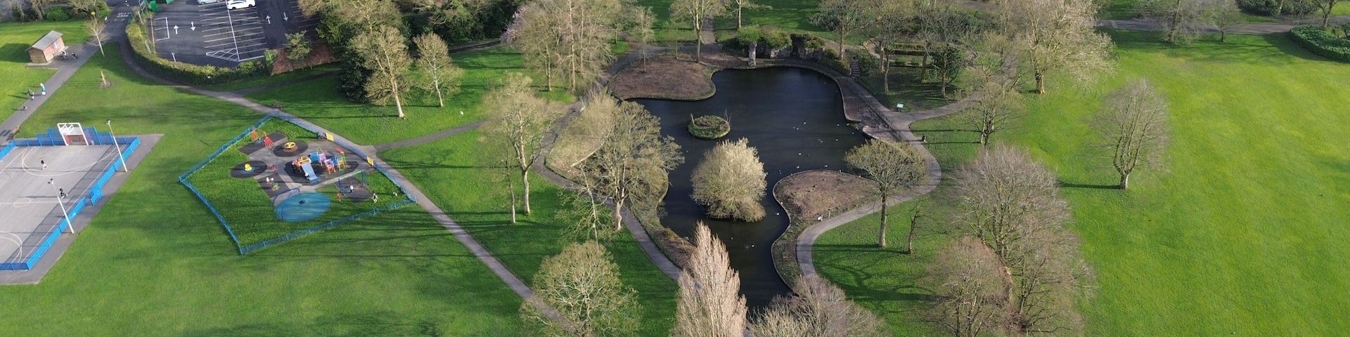 Vista aérea de um parque com lago, quadras de tênis e edifícios residenciais.
