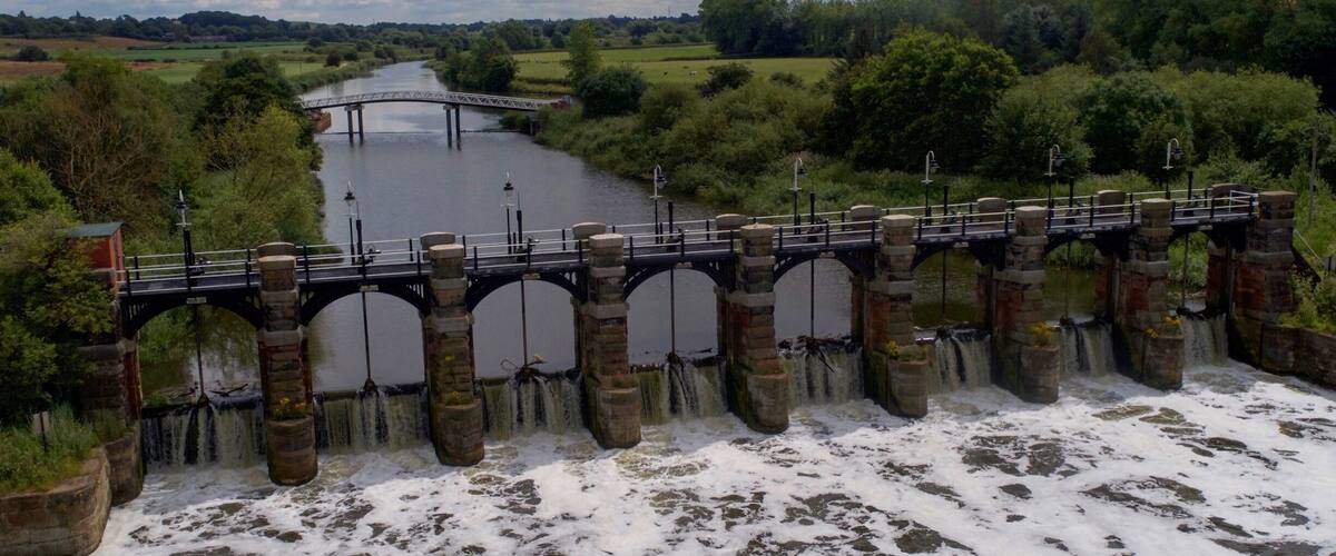 A stone bridge over a river with a dam releasing water.