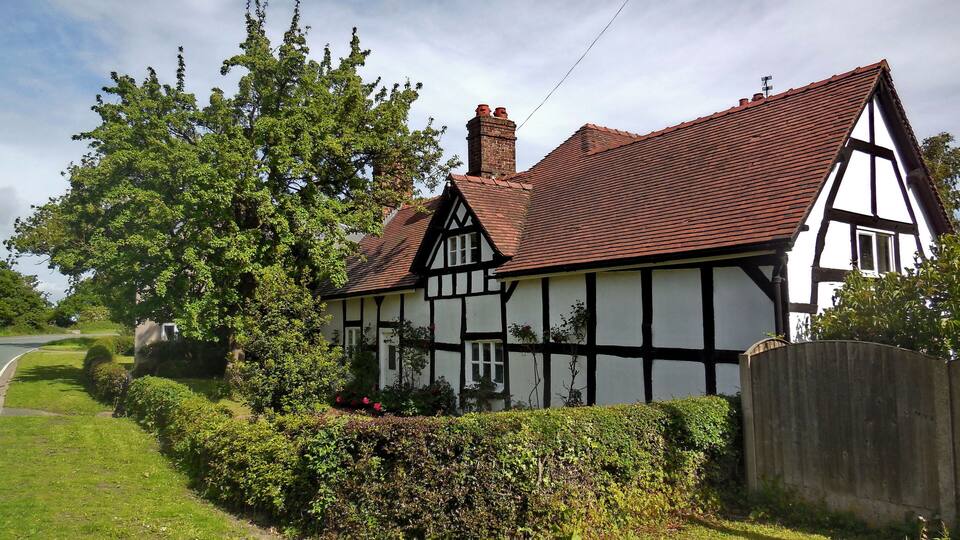 A Tudor-style house with a red-tiled roof, surrounded by lush greenery and a wooden fence.