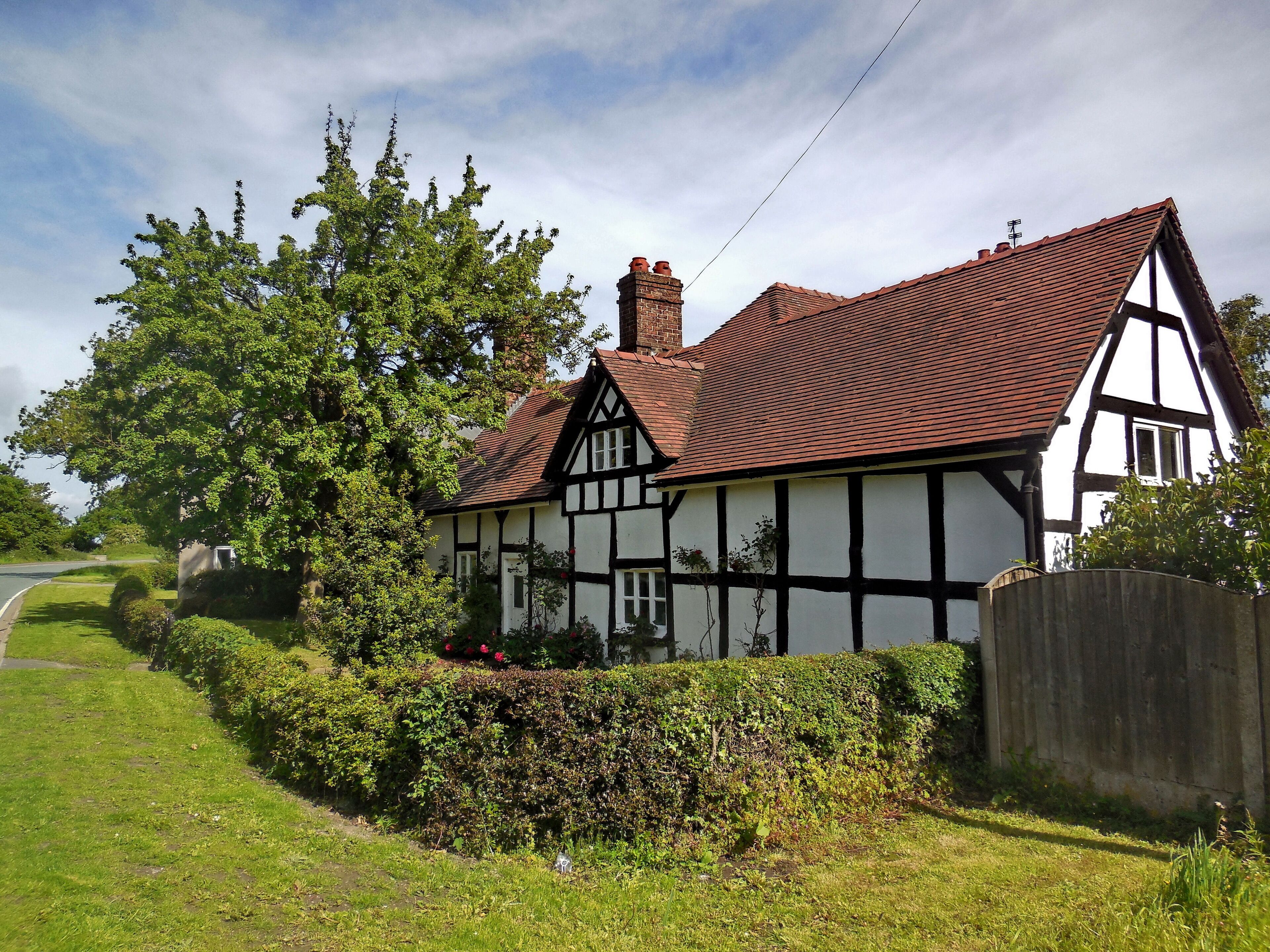A Tudor-style house with a red-tiled roof, surrounded by lush greenery and a wooden fence.