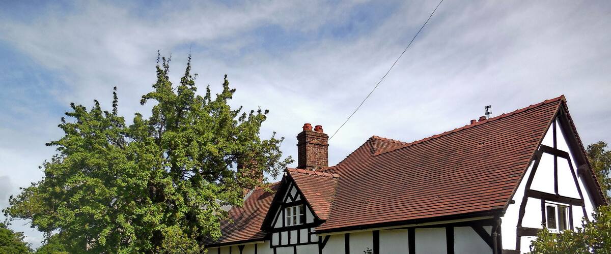A Tudor-style house with a red-tiled roof, surrounded by lush greenery and a wooden fence.