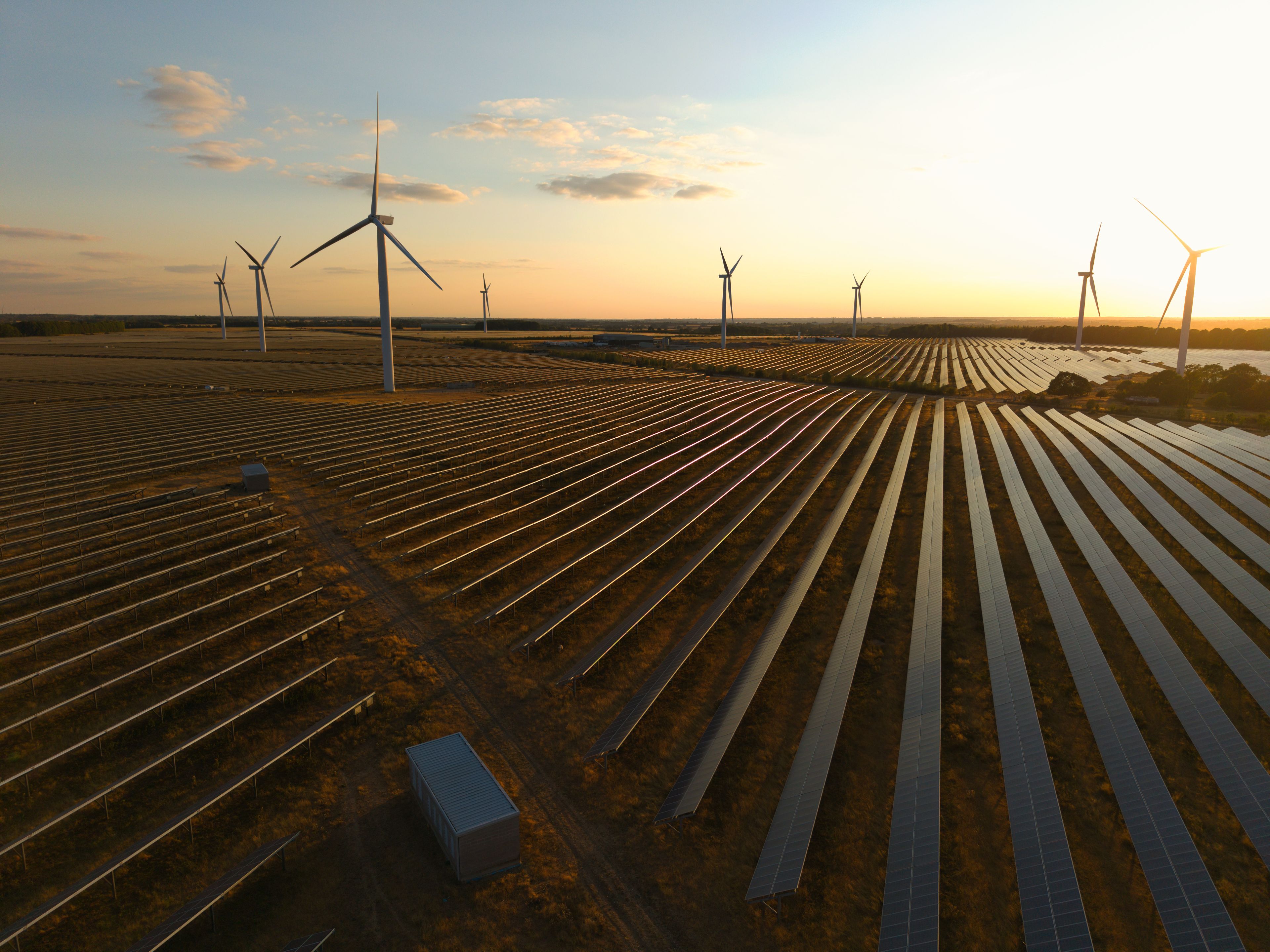 A solar farm with rows of solar panels and wind turbines in the background.
