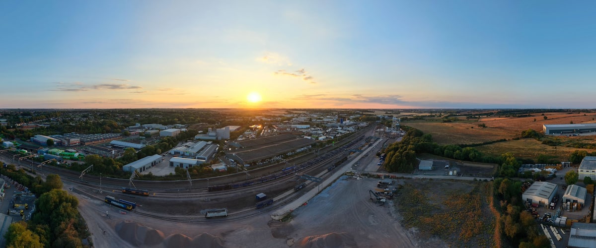 Aerial view of Wellingborough sidings freight terminal with railway tracks, industrial buildings, and landscape under sunset light in Wellingborough, England, United Kingdom.