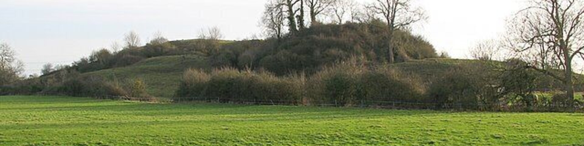 Fenny Castle Motte and Bailey Fenny Castle is a motte and bailey castle set on a small natural hill. The north west end of the hill has been scarped into a steep-sided conical to form a motte, while the south east end has been levelled to create a narrow bailey. Digging in the castle unearthed a wall which defended the summit, as well as iron rings, an iron implement and pottery. In C19 it is recorded that part of the slope at the north west end of the hill was removed to enable easier access around it. In the process the remains of 20 skeletons, possibly of a period predating the construction of the castle, were removed. The river Sheppey can be seen in the foreground.