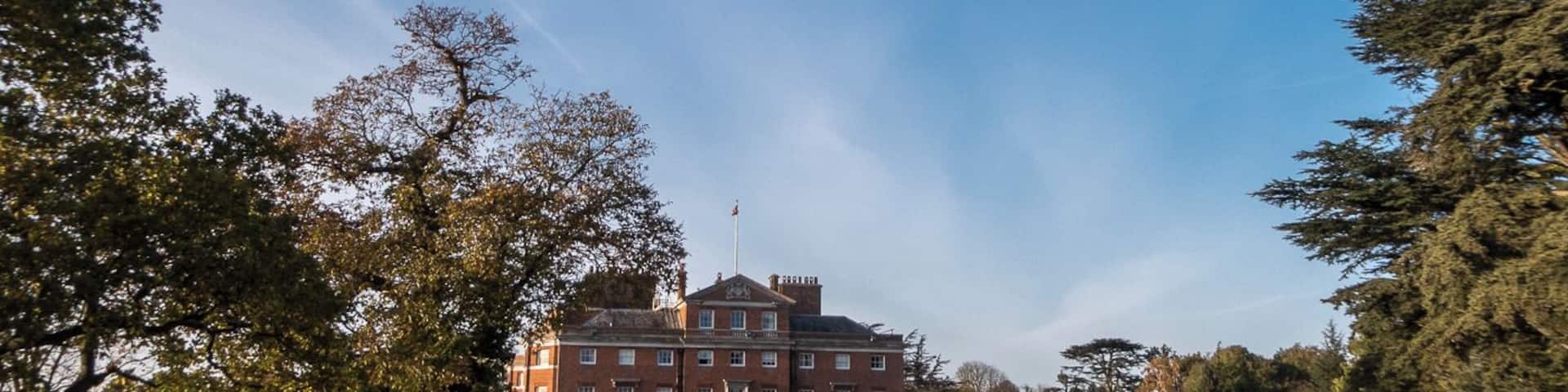 A large brick building with a flag on top, surrounded by trees and a well-maintained lawn.