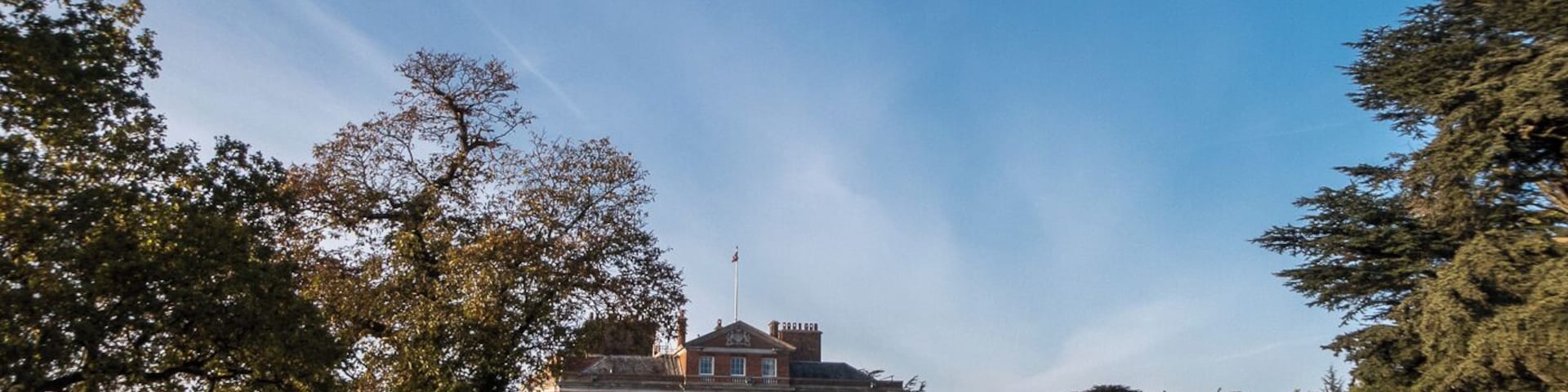 Um edifício grande de tijolos com uma bandeira no topo, rodeado por árvores e um gramado bem cuidado.