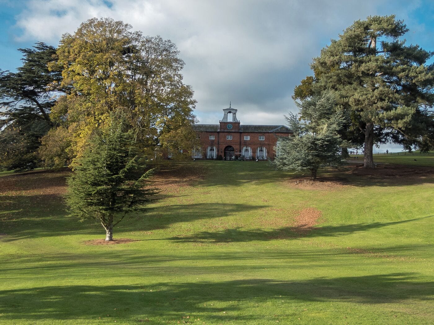 A large brick building with a clock tower, surrounded by a grassy field and trees.