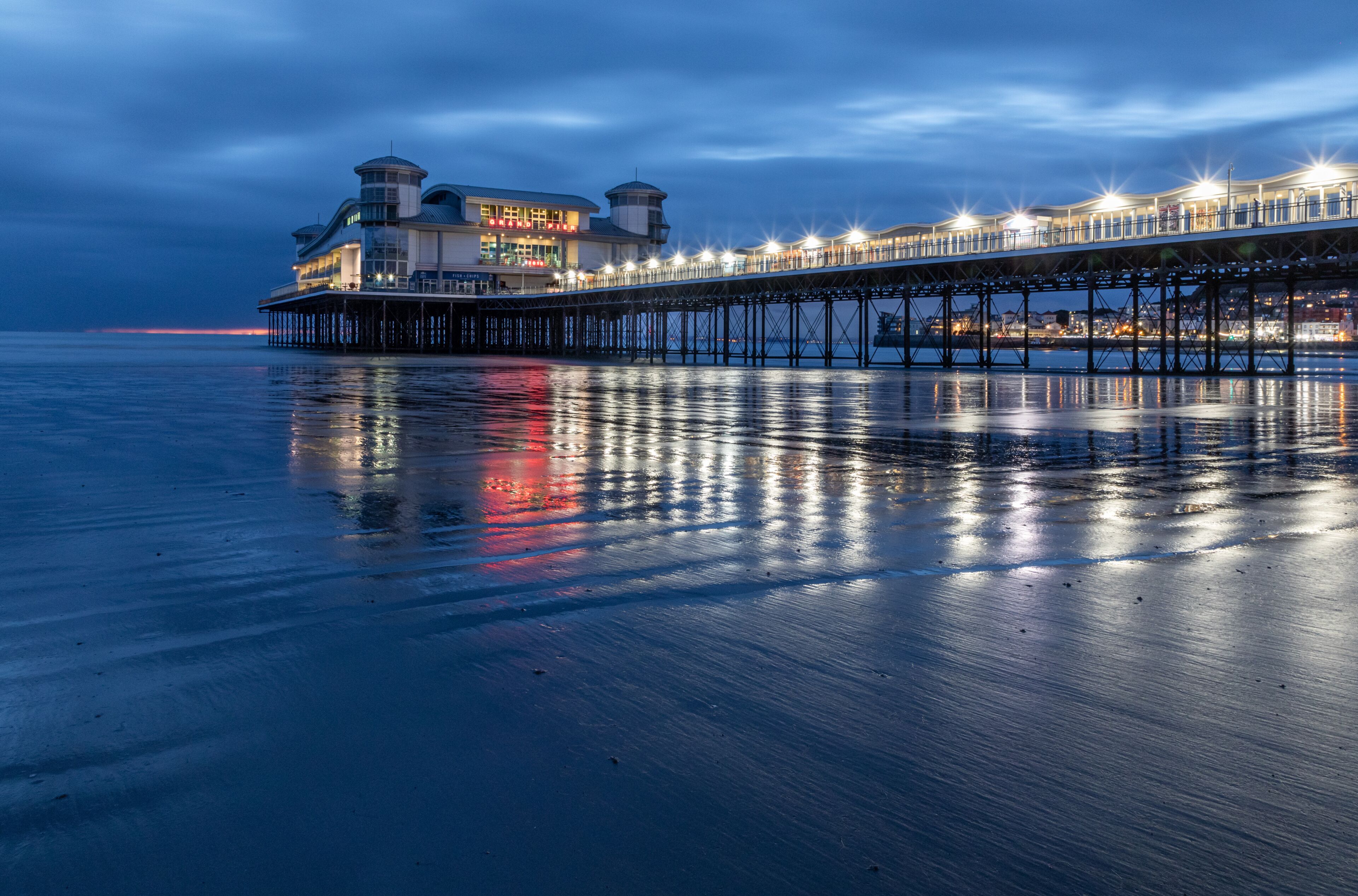 A pier extending into the water with a building on the left and lights reflecting on the water.