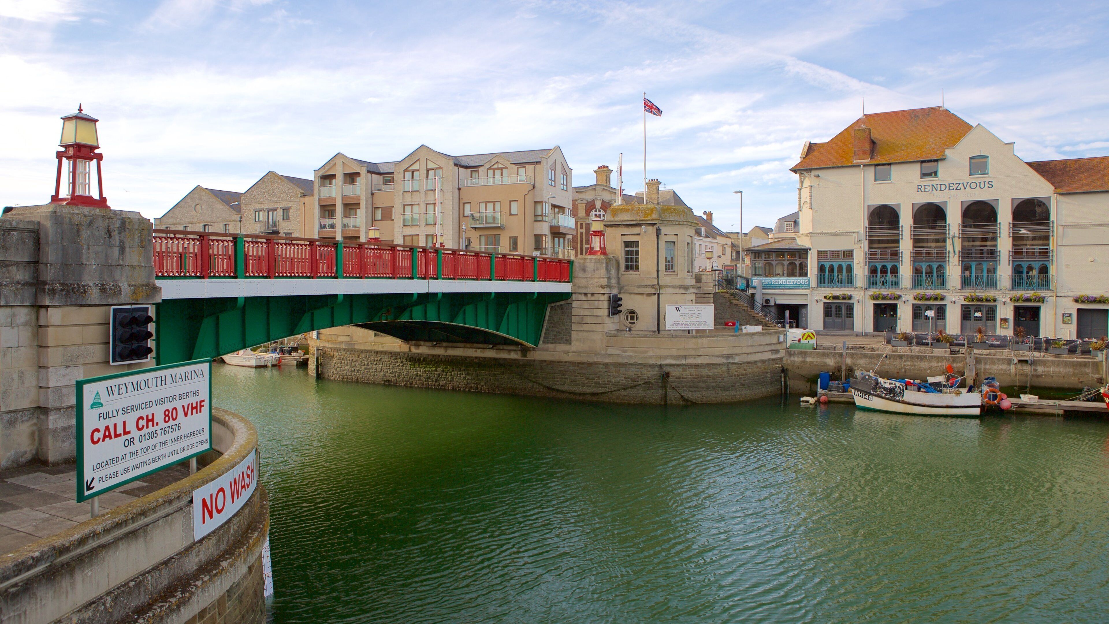 A green bridge over a river with boats, a lighthouse, and buildings including one labeled "RENDEZVOUS".