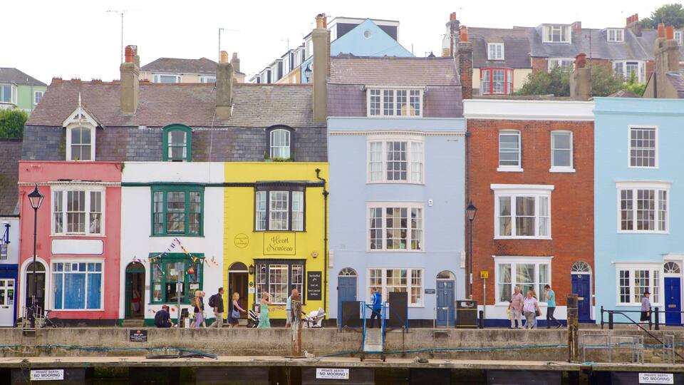 Colorful buildings along a waterfront with people walking and a sign indicating 'Private Berth No Mooring'.
