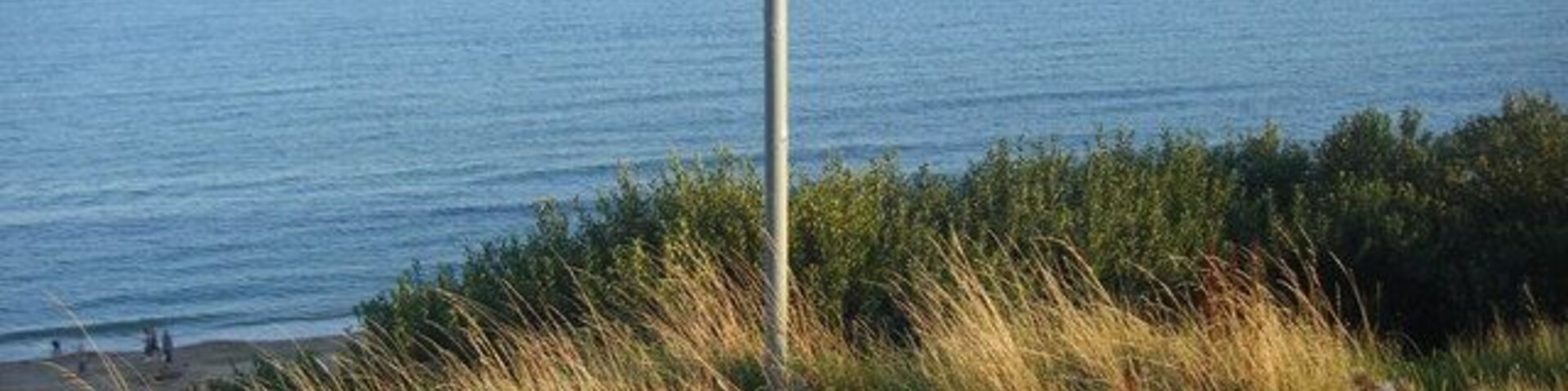 Señal de advertencia sobre acantilados peligrosos y una playa con gente al fondo.